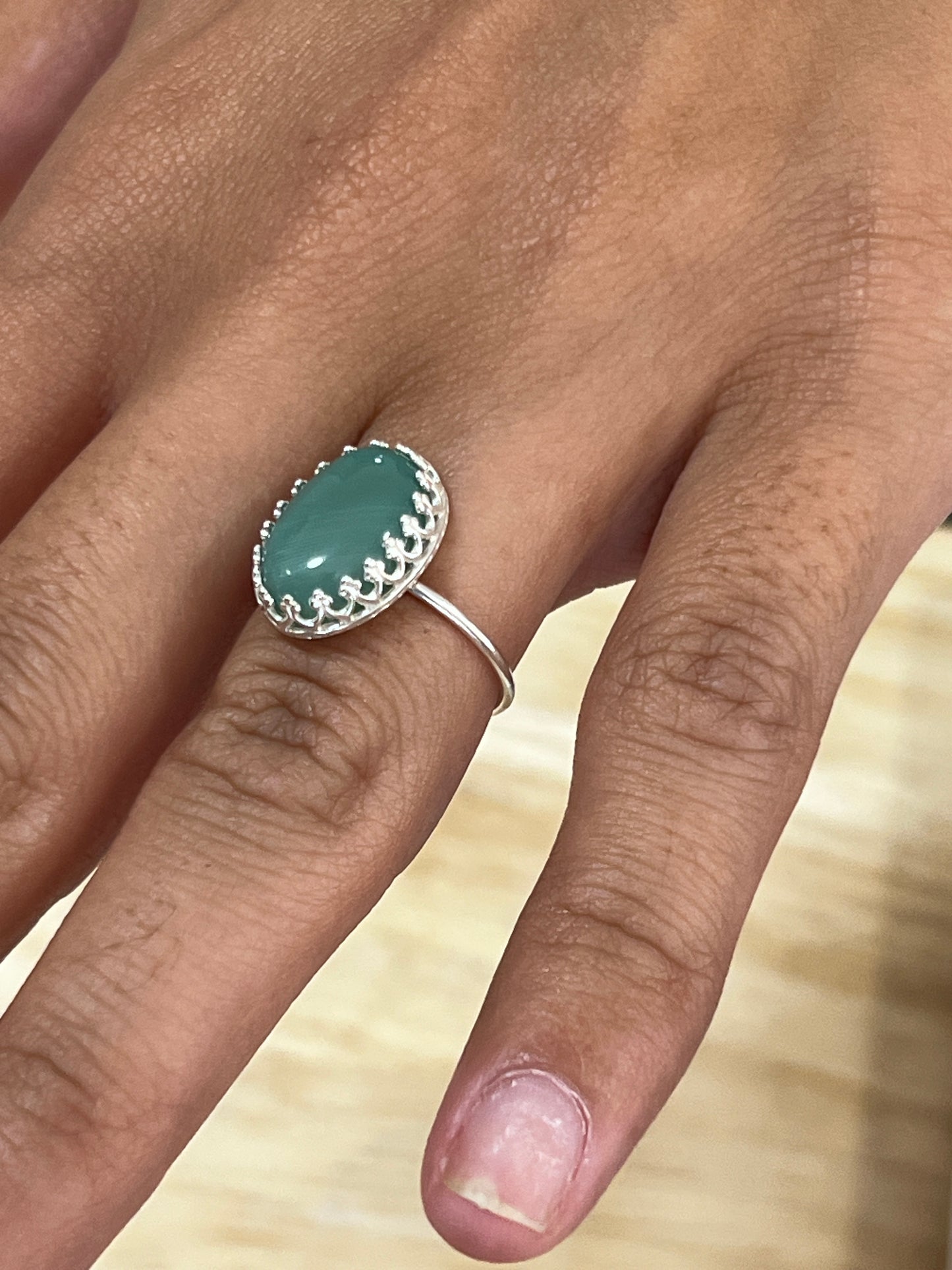 Silver ring with a green stone on a finger against a neutral background