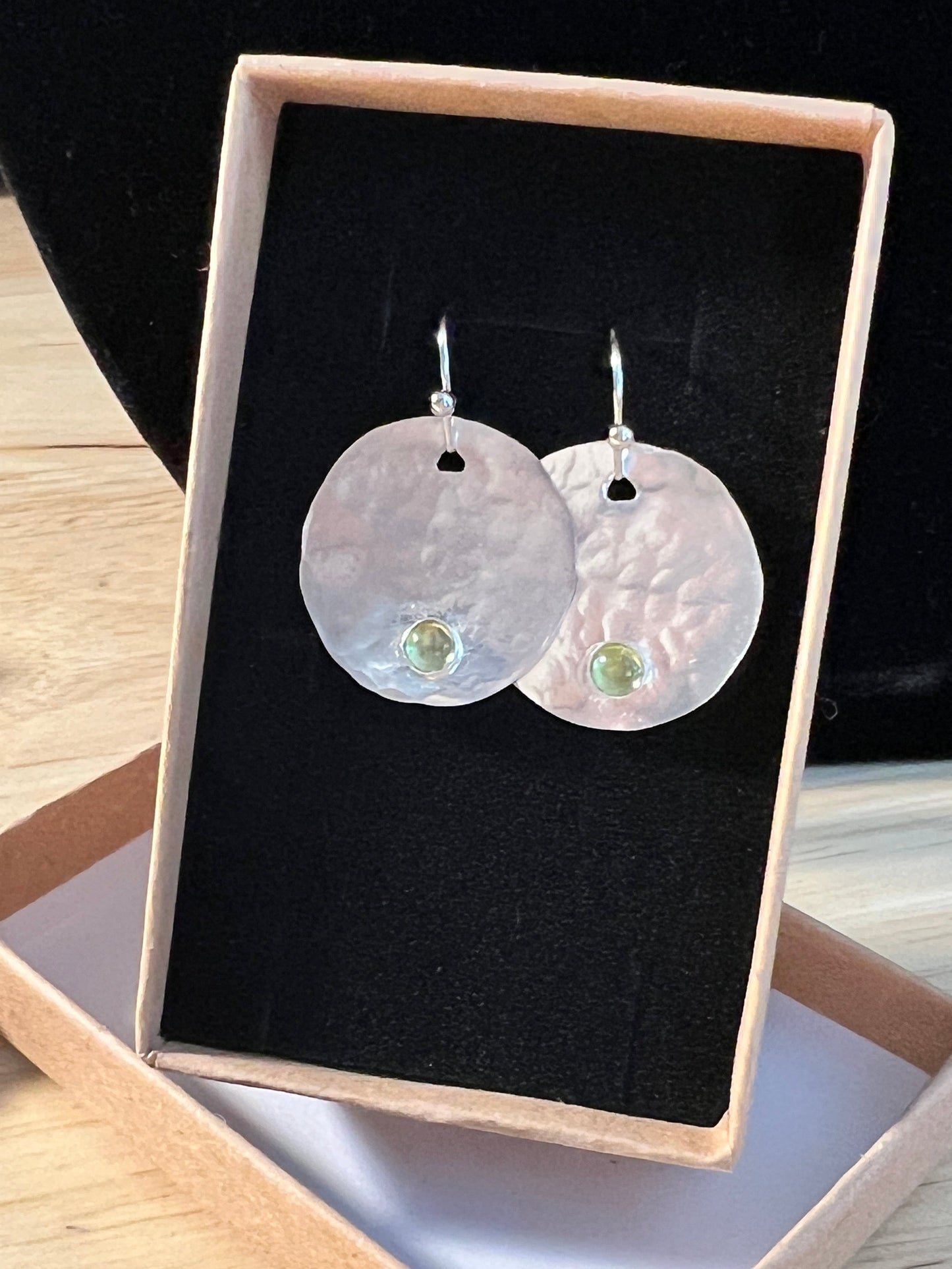 A pair handmade sterling silver circle dangle earrings made of round, sterling silver hammered discs and small green gemstone accents. 