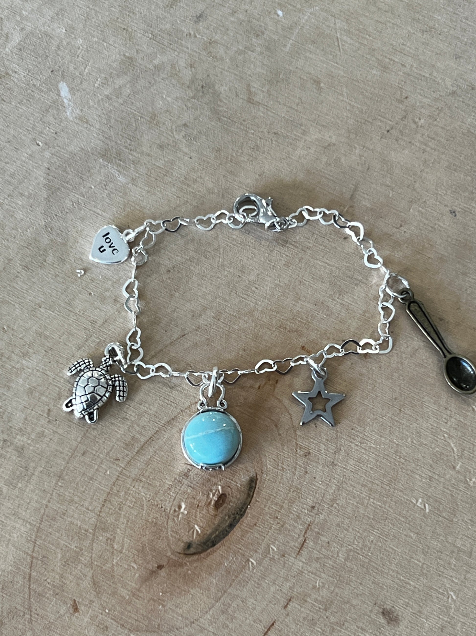 A silver charm bracelet with multiple charms including a heart, a turtle, and a gemstone