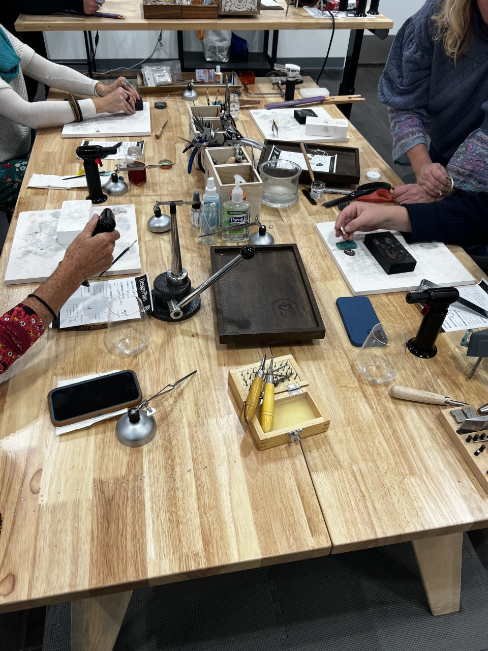 People making jewelry at a table with tools and materials on a wooden surface